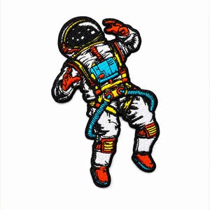 May include: An embroidered patch featuring an astronaut in a white spacesuit with black, red, yellow, and blue accents. The astronaut is depicted in a floating pose with a black helmet visor, a blue chest pack, and red gloves and boots.