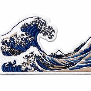 May include: An embroidered patch featuring a stylized depiction of a large ocean wave in shades of deep blue, light blue, and white, with a small mountain visible in the background. The design is outlined with a thick white border and textured stitching.