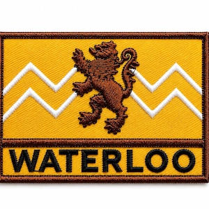 Puede incluir: Un parche rectangular bordado con fondo amarillo y un emblema de león marrón en el centro. Una línea blanca en zigzag cruza horizontalmente el parche. La palabra WATERLOO está bordada en letras mayúsculas negras en la parte inferior.