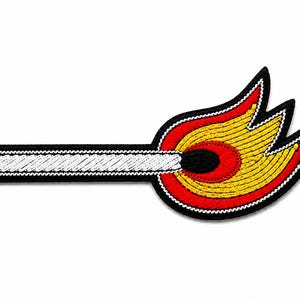 May include: An embroidered patch shaped like a lit matchstick. The matchstick has a white shaft with a black outline, a black head, and a flame depicted in vibrant yellow and red thread. The entire design is bordered by a thick black edge.