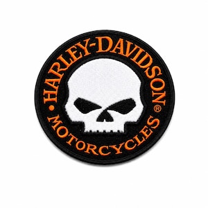 May include: A circular embroidered patch featuring a white skull centered on a black background. The text HARLEY-DAVIDSON MOTORCYCLES is stitched in orange thread in a circular border around the skull, with a registered trademark symbol.