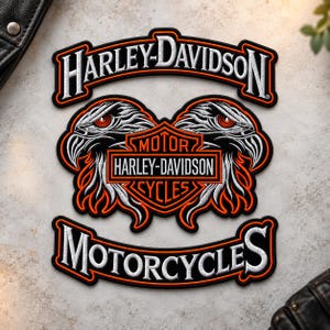 May include: A black, white, and orange embroidered patch featuring the Harley-Davidson logo. The design includes two eagle heads flanking a central shield with the text MOTOR HARLEY-DAVIDSON CYCLES, topped by an arched Harley-Davidson banner.