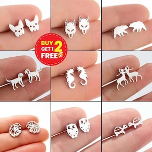 May include: A collection of nine pairs of silver-toned metal stud earrings featuring various animal shapes including a dog, wolf, bear, seahorse, deer, eagle, owl, and turtle, with a red circular graphic overlay stating BUY GET 1 FREE.