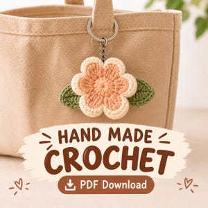 May include: A crochet flower keychain with a peach center and cream petals, accented by two green leaves, attached to a silver metal ring. The image features the text HAND MADE CROCHET and PDF Download with small heart icons on a beige bag.