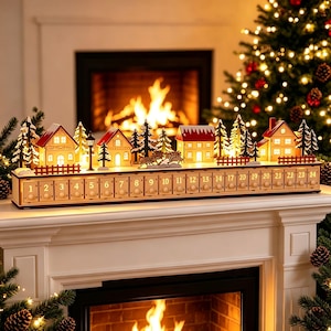 Könnte beinhalten: Ein hölzerner Adventskalender mit einer Miniatur-Dorfkulisse aus beleuchteten Häusern, Tannenbäumen und einem roten Zaun. Der Sockel enthält vierundzwanzig nummerierte Schubladen mit kleinen runden Knöpfen in einer horizontalen Reihe.