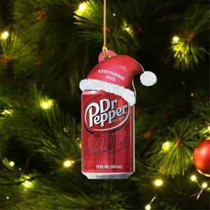 May include: A Dr Pepper soda can ornament featuring a red Santa hat with white trim. The hat is printed with the name Stephanie and the year 2025. The can displays the Dr Pepper logo, the number 23, and the text 12 FL OZ (355 mL) in white.