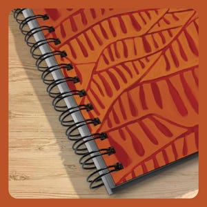 May include: A spiral-bound notebook featuring a vibrant orange cover decorated with a repeating pattern of dark red, leaf-like shapes. The black metal wire binding runs along the left side, securing the pages within the durable, colored cover.