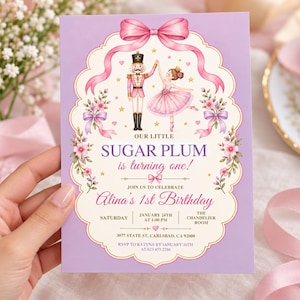 May include: A rectangular invitation card with a light purple border featuring a nutcracker and a ballerina illustration. Text reads: Our little Sugar Plum is turning one! Join us to celebrate Alina's 1st Birthday, Saturday, January 24th at 1:00 PM.