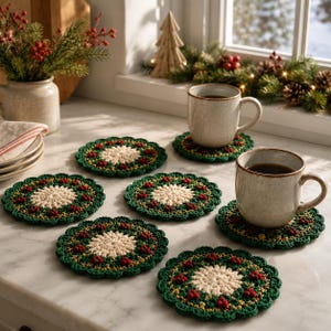 May include: A set of six round, crocheted coasters featuring a cream-colored center, a dark green border, and small red accents resembling berries. Two of the coasters are topped with speckled, light-colored ceramic mugs filled with dark liquid.