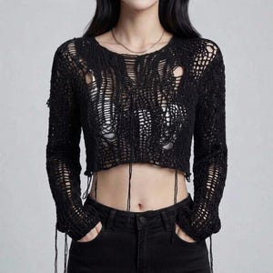 May include: A black long-sleeve crop top featuring a loose, open-knit crochet construction with a distressed, shredded appearance. The garment has a round neckline, long sleeves, and thin, dangling thread accents hanging from the hem and cuffs.