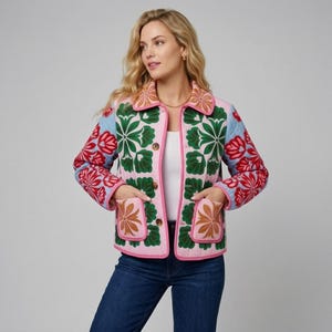 May include: A quilted jacket featuring a light pink base with a vibrant floral pattern in shades of green, red, and tan. The garment has a collared neckline, long sleeves, a button-front closure, and two front patch pockets with pink trim.
