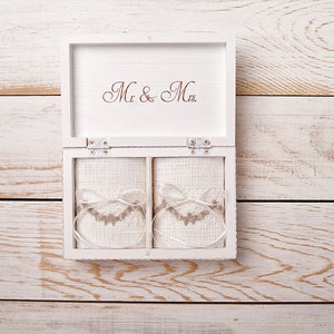 Pu&ograve; includere: Scatola di legno bianca con le parole "Mr. & Mrs." sul coperchio. La scatola &egrave; aperta e contiene due piccole buste di tessuto bianco con bordi marroni.