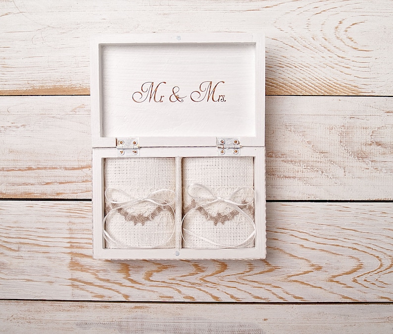 Pu&ograve; includere: Scatola di legno bianca con le parole "Mr. & Mrs." sul coperchio. La scatola &egrave; aperta e contiene due piccole buste di tessuto bianco con bordi marroni.