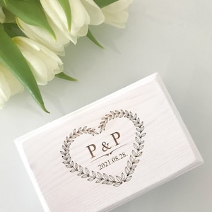 Pu&ograve; includere: Scatola di legno bianca con un design a forma di cuore inciso con le iniziali "P&P" e la data "2021.08.28."