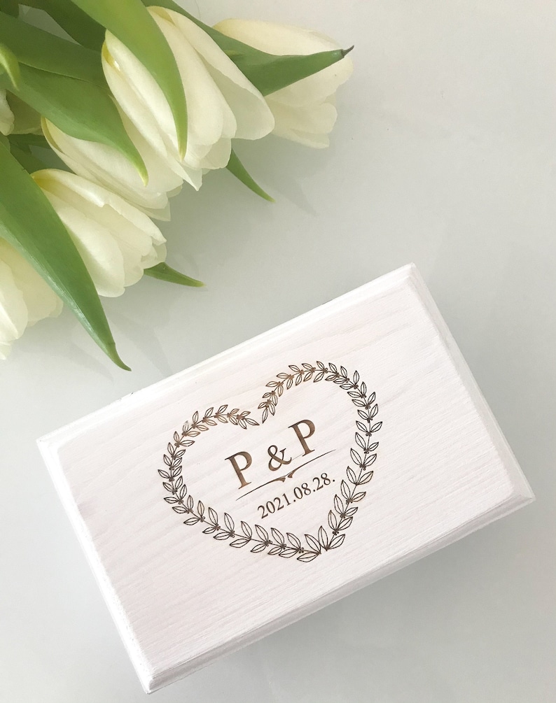 Pu&ograve; includere: Scatola di legno bianca con un design a forma di cuore inciso con le iniziali "P&P" e la data "2021.08.28."