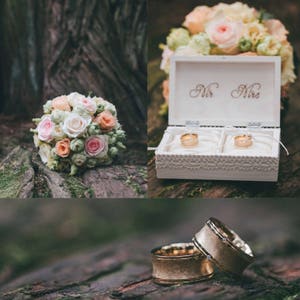 Pu&ograve; includere: Due fedi nuziali d'oro su una superficie di legno. Le fedi sono accanto a una scatola bianca con le parole "Mr. Mrs." sul coperchio. Sullo sfondo c'&egrave; un bouquet di fiori rosa e bianchi.