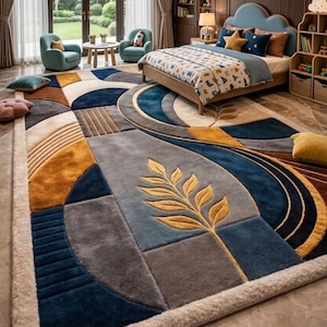 May include: A large rectangular area rug featuring a geometric pattern with circular and linear segments in shades of navy blue, mustard yellow, gray, and cream. The design includes a central stylized leaf motif and a thick, textured border.