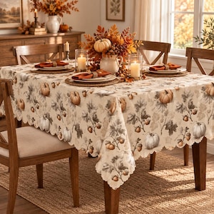 May include: A rectangular tablecloth featuring a repeating pattern of pumpkins, acorns, and oak leaves in muted brown and grey tones on a cream background, with a scalloped edge, covering a wooden dining table set for a meal with place settings.