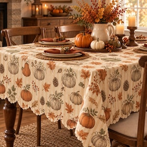 May include: A rectangular tablecloth with a scalloped edge featuring a repeating pattern of pumpkins, autumn leaves, and pinecones on a cream and beige striped background. The fabric displays various shades of orange, green, and brown illustrations.