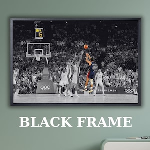 May include: A black-framed wall art print featuring a black and white photograph of a basketball game in progress. A player in a colored jersey jumps to shoot the ball toward the hoop, while other players and a large crowd are visible in the background.