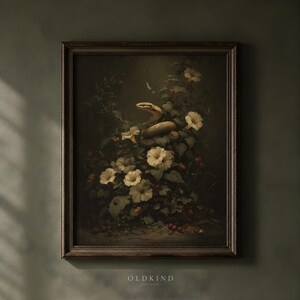 May include: A framed wall art print featuring a dark, moody botanical scene with a coiled snake nestled among white flowers and green foliage. The artwork is set within a dark brown frame and includes the text OLD KIND at the bottom center.