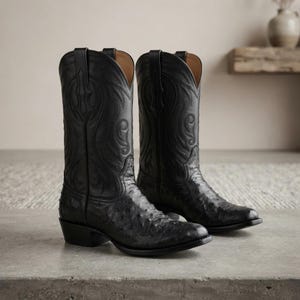 Könnte beinhalten: Ein Paar schwarze Leder-Cowboystiefel mit einer texturierten Musterung am Fußteil und aufwendigen, farblich abgestimmten Ziernähten am hohen Schaft. Die Stiefel haben eine spitz zulaufende Kappe, einen Blockabsatz und Zuglaschen am Schaft.