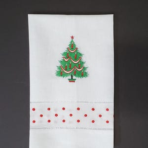 May include: White Christmas hand towel with an embroidered green Christmas tree design, adorned with red ornaments and a star on top. The bottom border features red polka dots. A festive holiday accent.