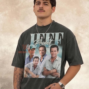 Op de afbeelding: Een antracietgrijs T-shirt met korte mouwen en een grote grafische print van Jeff Probst in verschillende poses. De tekst "JEFF" staat in grote witte letters boven de naam "Probst" in een cursief lettertype.