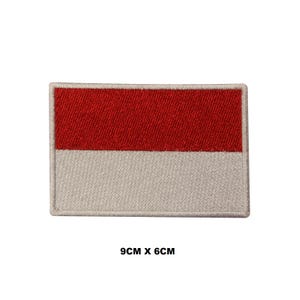 May include: A rectangular embroidered patch featuring a horizontal bicolor design with a red upper half and a white lower half. The patch has a stitched border and measures 9 cm by 6 cm as indicated by the text printed below the object.