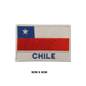 May include: A rectangular embroidered patch featuring the flag of Chile with a blue square containing a white star, a white horizontal stripe, and a red horizontal stripe. Below the flag, a white bar displays the text CHILE in blue. Measures 9cm x 6cm.