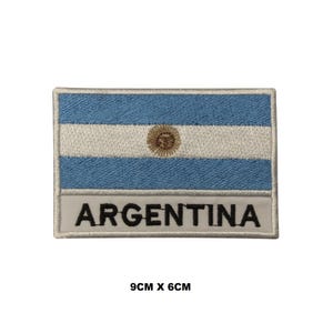 Può includere: Una toppa rettangolare ricamata raffigurante la bandiera dell'Argentina con due strisce orizzontali azzurre e una striscia centrale bianca contenente un sole dorato. Sotto la bandiera, la parola ARGENTINA è ricamata in nero, misura 9cm x 6cm.