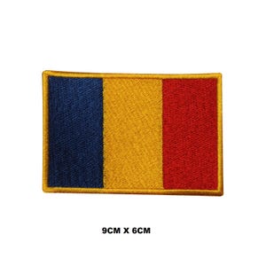 May include: A rectangular embroidered patch featuring the vertical tricolor flag of Romania with blue, yellow, and red stripes, bordered by a gold thread edge. The patch measures 3.54 inches by 2.36 inches as indicated by the text 9CM X 6CM.