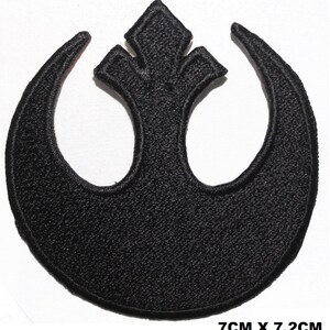 May include: A black embroidered patch featuring the Rebel Alliance symbol, a stylised starbird emblem with a central vertical point and two curved wings. The patch measures 7cm by 7.2cm, as indicated by the text printed at the bottom right corner.