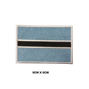May include: A rectangular embroidered patch featuring the flag of Botswana, consisting of a light blue field with a central black horizontal stripe bordered by two thin white stripes. The patch measures 9cm x 6cm as indicated by the text.