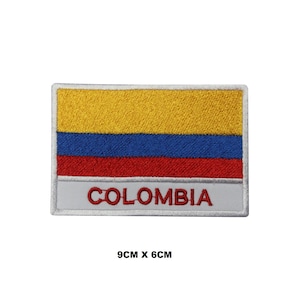 Può includere: Una toppa rettangolare ricamata che presenta le strisce orizzontali gialla, blu e rossa della bandiera colombiana. Sotto le strisce, una fascia bianca mostra la parola COLOMBIA in lettere maiuscole rosse. La toppa misura 9 cm per 6 cm.