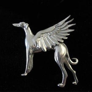 May include: A silver-toned brooch depicting a stylized greyhound with wings. The wings are spread out and have a detailed feather design.