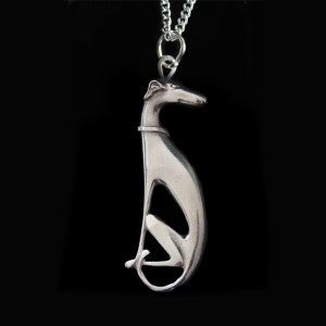 Puede incluir: Un collar con un colgante de plata con un diseño de galgo estilizado. El colgante es detallado y tiene un acabado liso y pulido.