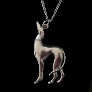 May include: Silver Greyhound pendant necklace. The pendant is a detailed, realistic depiction of a Greyhound dog standing on all four legs with its head tilted up. The necklace is on a silver chain.