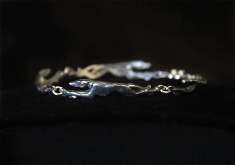 以下が含まれることがあります： チェーンのデザインで、反対方向に走る2匹のグレイハウンドの犬のフィギュアが特徴のシルバーブレスレットです。