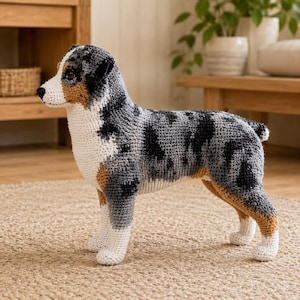Può includere: Un animale di peluche realizzato all'uncinetto che raffigura un cane pastore australiano. La figura presenta un mantello maculato in filato grigio, nero e bianco con accenti color cuoio sul muso e sulle zampe, in piedi su quattro zampe con petto bianco.