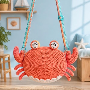 May include: A round, orange crocheted bag shaped like a crab, featuring two white and black eyes on top, two raised claws on the sides, and six small legs. The bag has a white scalloped bottom edge and an adjustable strap with blue and orange patterns.