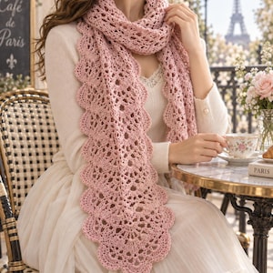 May include: A long, light pink crochet scarf featuring an intricate openwork pattern with a scalloped edge. The scarf is draped around the neck and hangs down the front, showcasing a detailed, repeating lace-like design throughout the fabric.