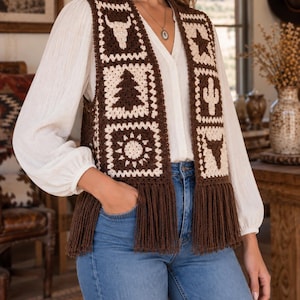May include: A brown and cream crochet vest featuring square motifs with patterns of a bull skull, a pine tree, a sun, a star, and a cactus. The sleeveless garment has a V-neckline and a long fringe trim along the bottom hem edge.