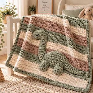 May include: A chunky crochet blanket featuring horizontal stripes in sage green, cream, and dusty rose. A large, three-dimensional sage green dinosaur appliqué with a long neck and closed eyes is attached to the center of the textured fabric.