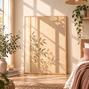 Puede incluir: Una gran pieza de arte mural rectangular con superficie beige claro, enmarcada en madera natural. La superficie muestra una sombra oscura y nítida de ramas de plantas con hojas proyectada por la luz solar, creando un patrón botánico de alto contraste.