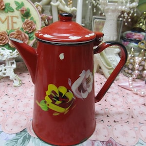 May include: Red enamel teapot with a white lid and painted floral design. The teapot has a black handle and spout.