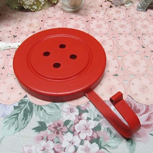 May include: Red metal button-shaped hook with four holes. The hook is attached to a red metal base.