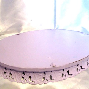 Pu&ograve; includere: Un porta torta ovale color lavanda con un bordo decorativo a festoni. Il supporto &egrave; in metallo e ha una superficie liscia e verniciata.