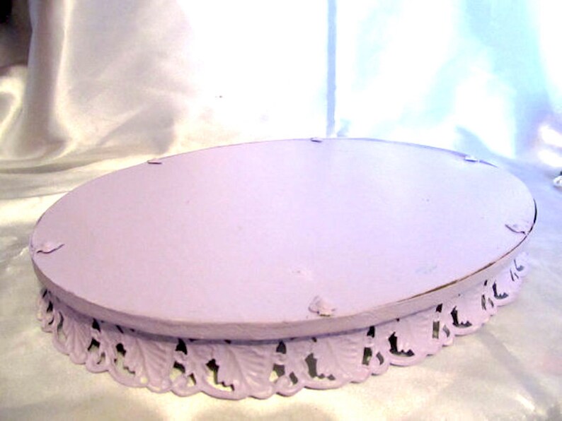 Pu&ograve; includere: Un porta torta ovale color lavanda con un bordo decorativo a festoni. Il supporto &egrave; in metallo e ha una superficie liscia e verniciata.