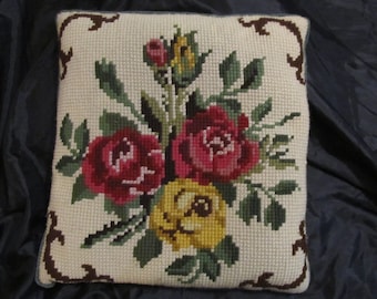 May include: A white pillow with a floral embroidery design. The pillow features red, yellow, and green roses with brown stems and leaves.